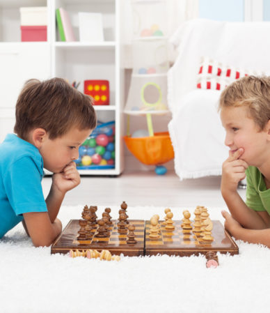 Two boys playing chess laying on the floor and thinking hard